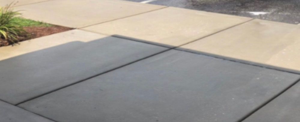 Gray and tan concrete sidewalk with a patch of green grass and a light mist.