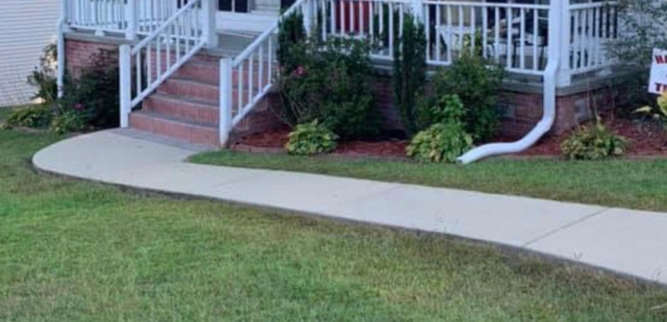 A house with a white porch and a curved sidewalk leading to the steps. Green grass surrounds it.