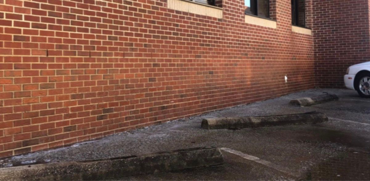 Brick wall, parking area with wheel stops, and partial view of a car.