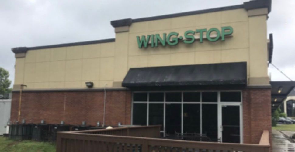 Wingstop restaurant exterior with green sign, beige walls, and brown trim. Dark awning over entrance.