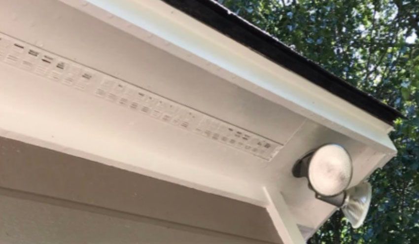 White painted eaves with a floodlight, a black rain gutter, and visible ventilation.