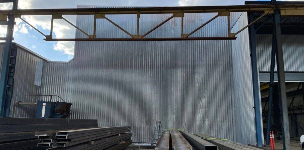 A metal industrial building with metal beams, gray corrugated walls, and stacks of metal.