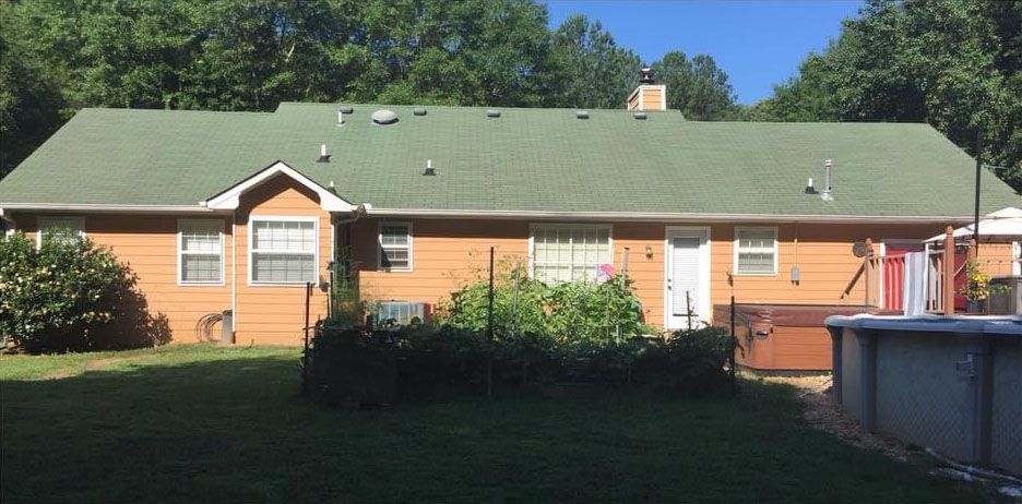 Backyard view of a house with a green roof, garden, and a pool on a sunny day.