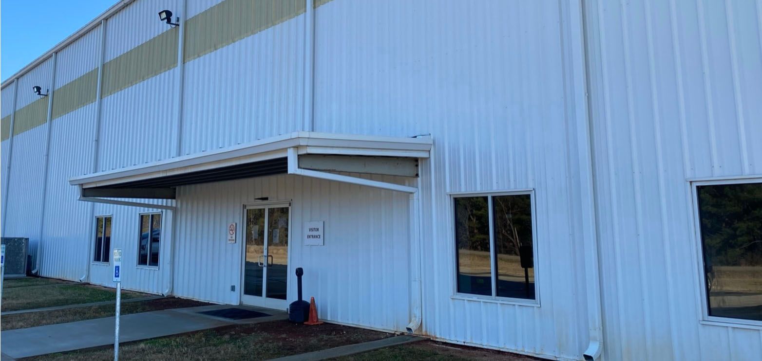 Exterior view of a white industrial building with a covered entrance and windows.
