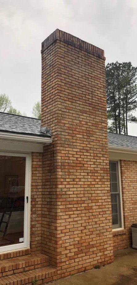 Brick chimney attached to a brick house under an overcast sky.