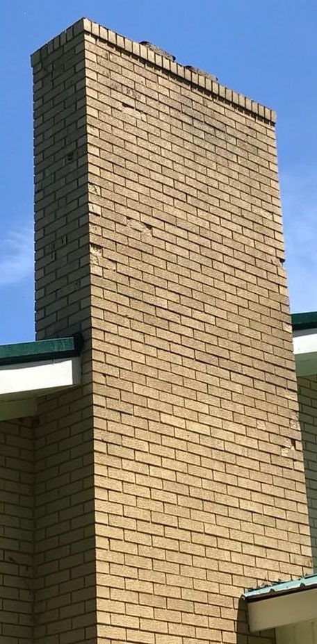 Tall brick chimney against a blue sky, part of a building with a green roof.