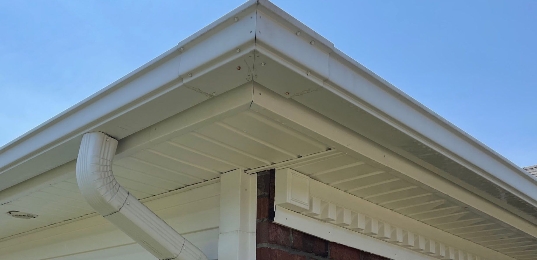 Corner of a building with white siding, soffit, and gutter against a blue sky.