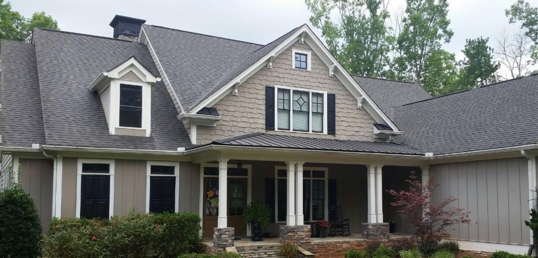 Tan and gray house with porch and dark roof. Trees in the background.