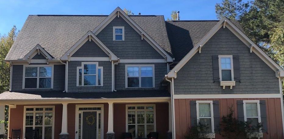 Two-story house with gray and reddish-brown siding, blue sky.