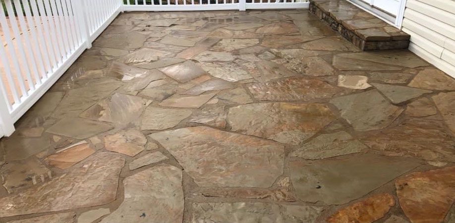 Stone patio with white railing and house siding.