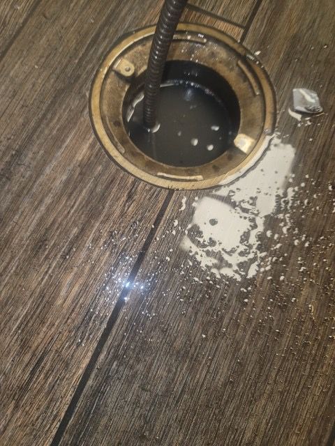 A drain on a wooden floor with water coming out of it.