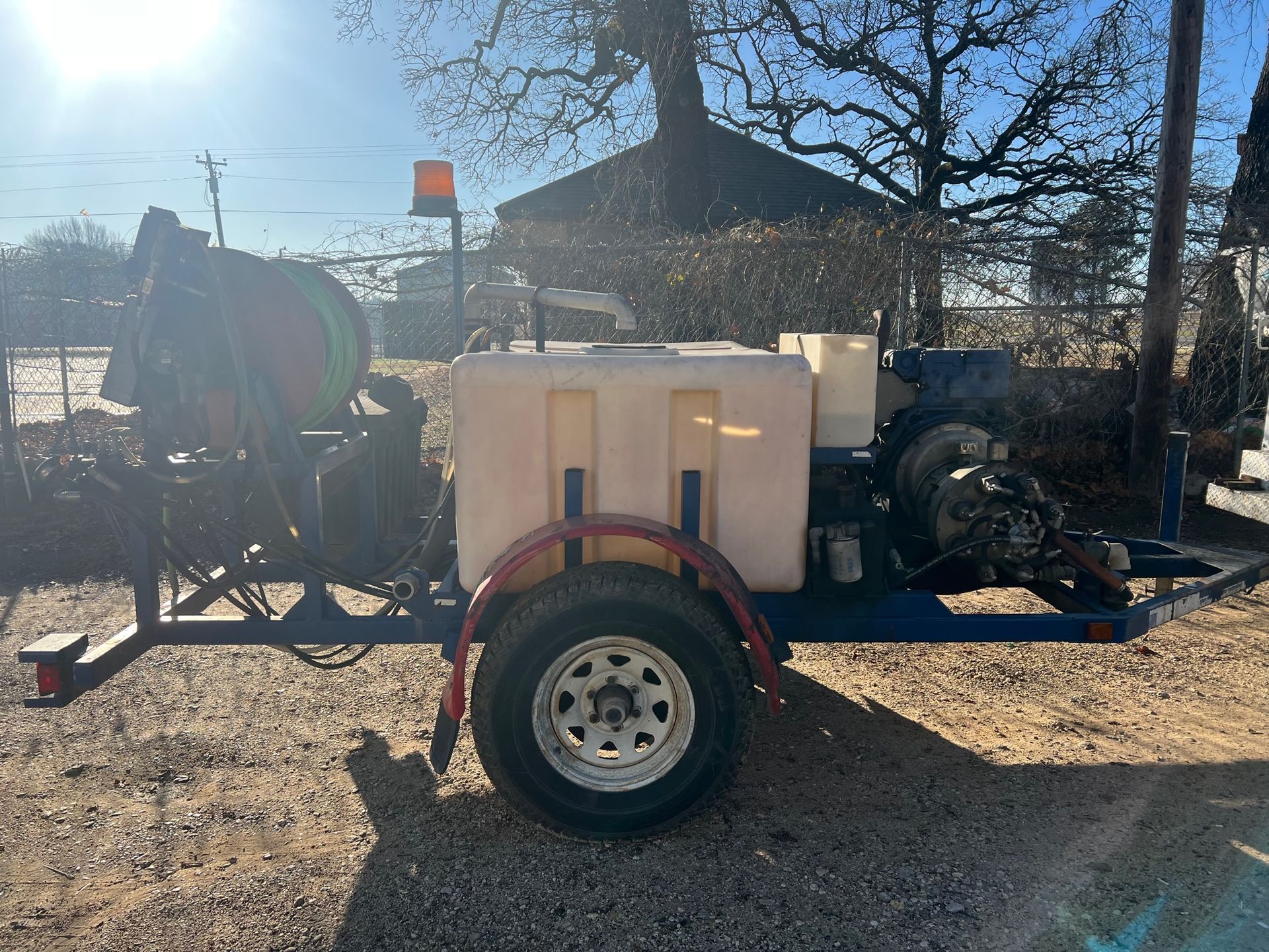 A trailer with a hose attached to it is parked in a gravel lot.
