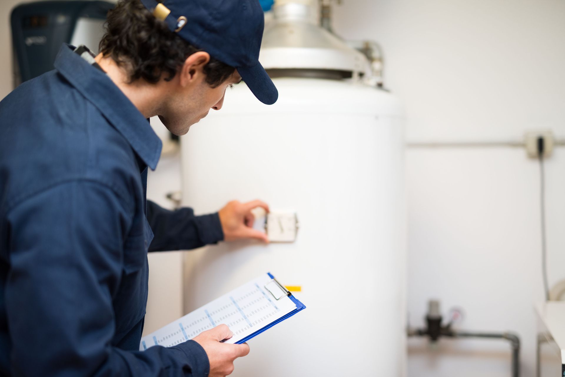 A man is looking at a water heater while holding a clipboard.