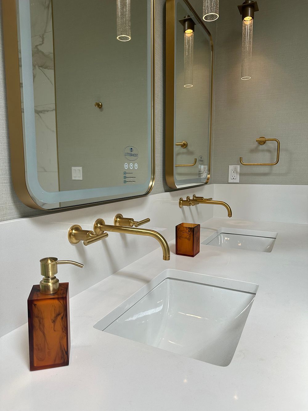 Bathroom with white countertop, gold fixtures, amber soap dispenser, two mirrors.
