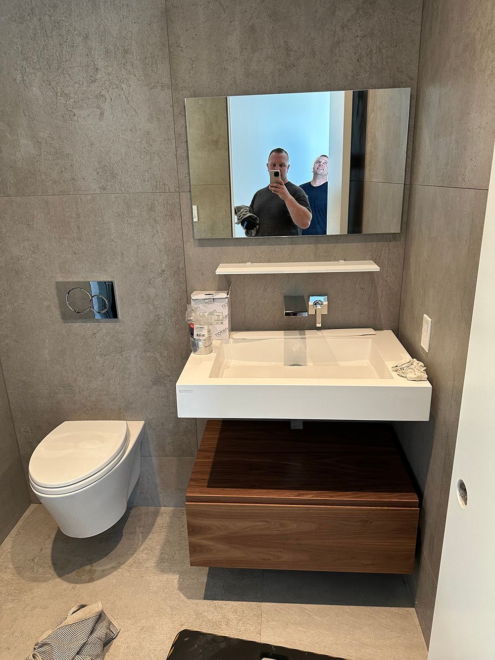 Modern bathroom with floating sink, toilet, and wood cabinet. Gray tiled walls.