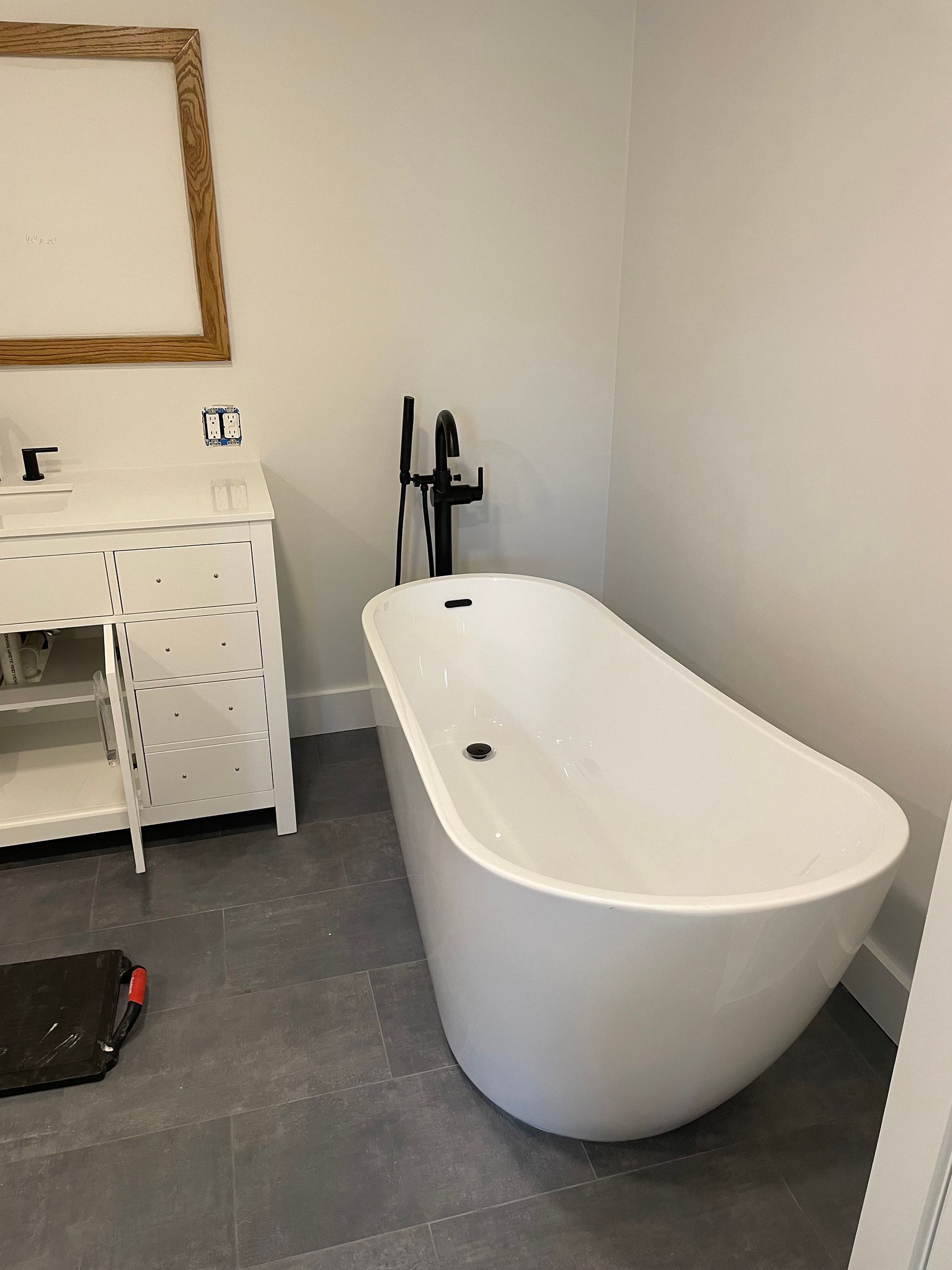 Modern bathroom with a white standalone tub, black faucet, white vanity, and gray tiled floor.
