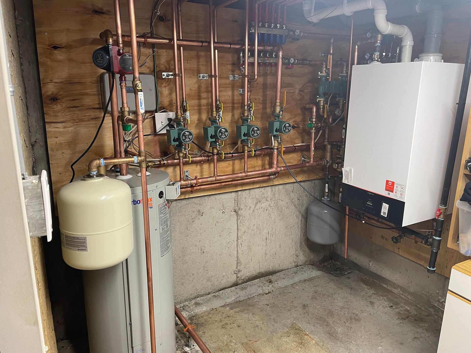 Copper pipes and a white boiler in a basement room, with other mechanical components.