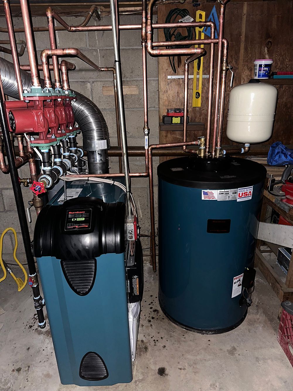 A blue boiler and water heater with copper pipes in a basement.