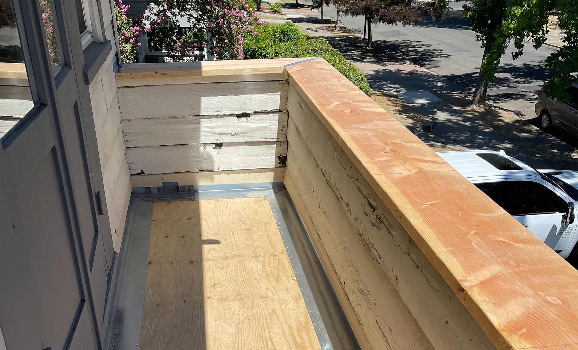 Narrow balcony under construction with unfinished wood railings and floor, viewed from above.