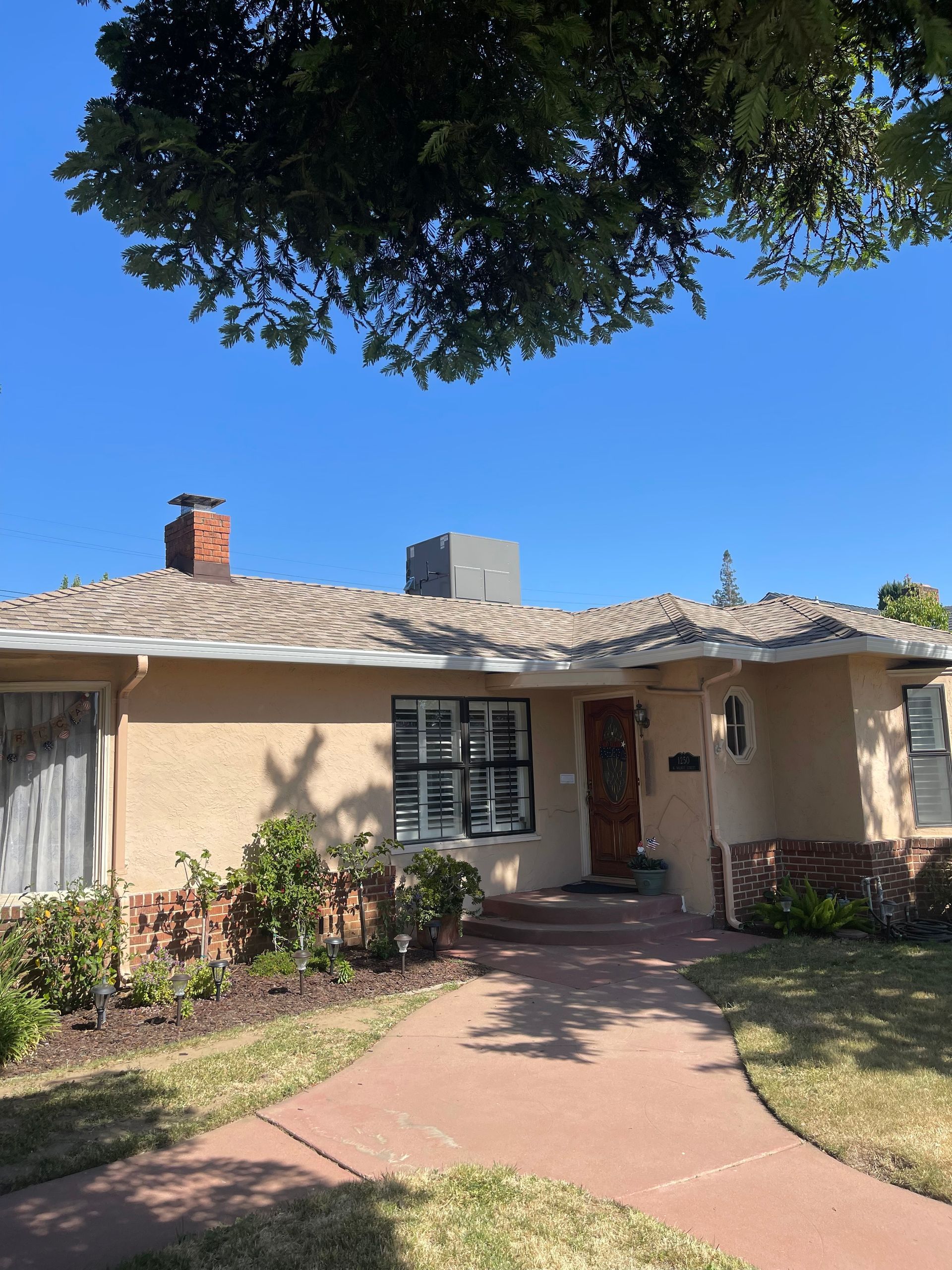 Single-story beige house with a red walkway, front porch, and tree shade overhead