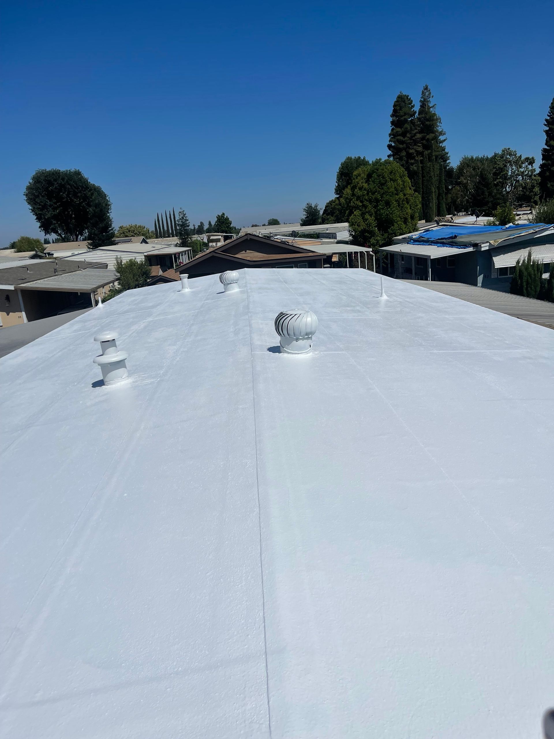 White rooftop under a clear blue sky, with vents and nearby trees and houses.