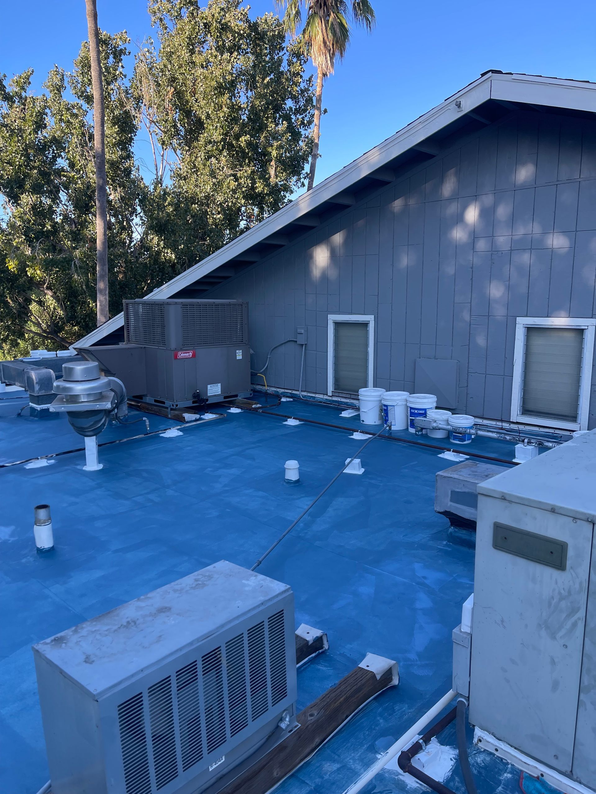 Roof under construction with blue tarp, HVAC units, and tools beside a gray building