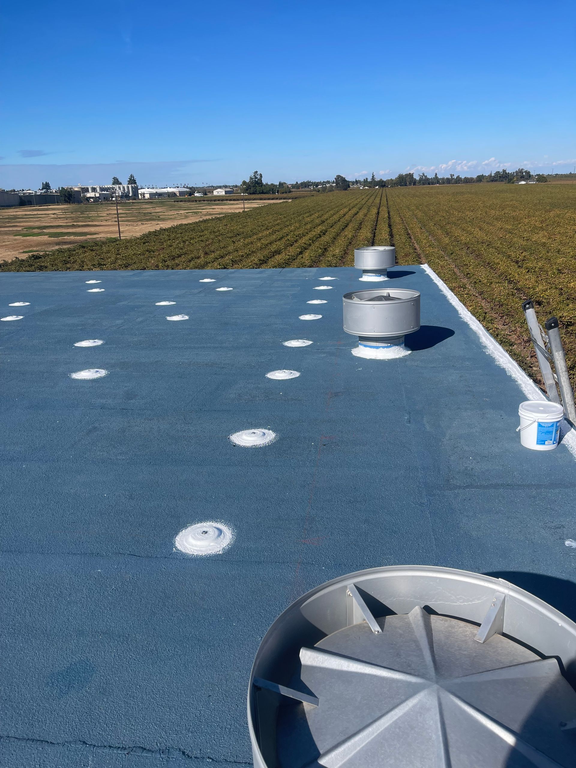 Blue rooftop with vents and white markers overlooking open farmland under a clear sky