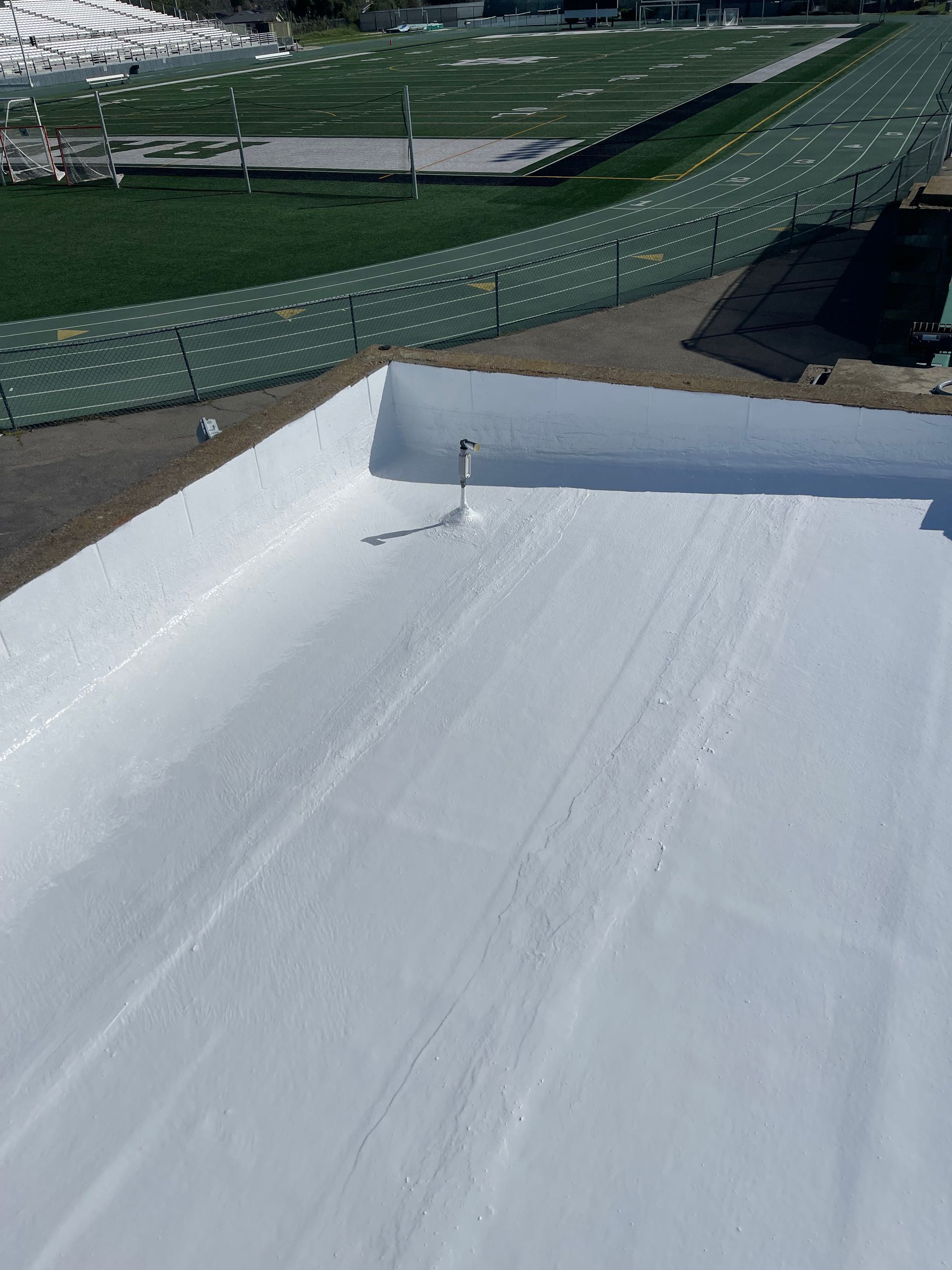 Snow-covered rooftop with a white surface and green bleachers in the background