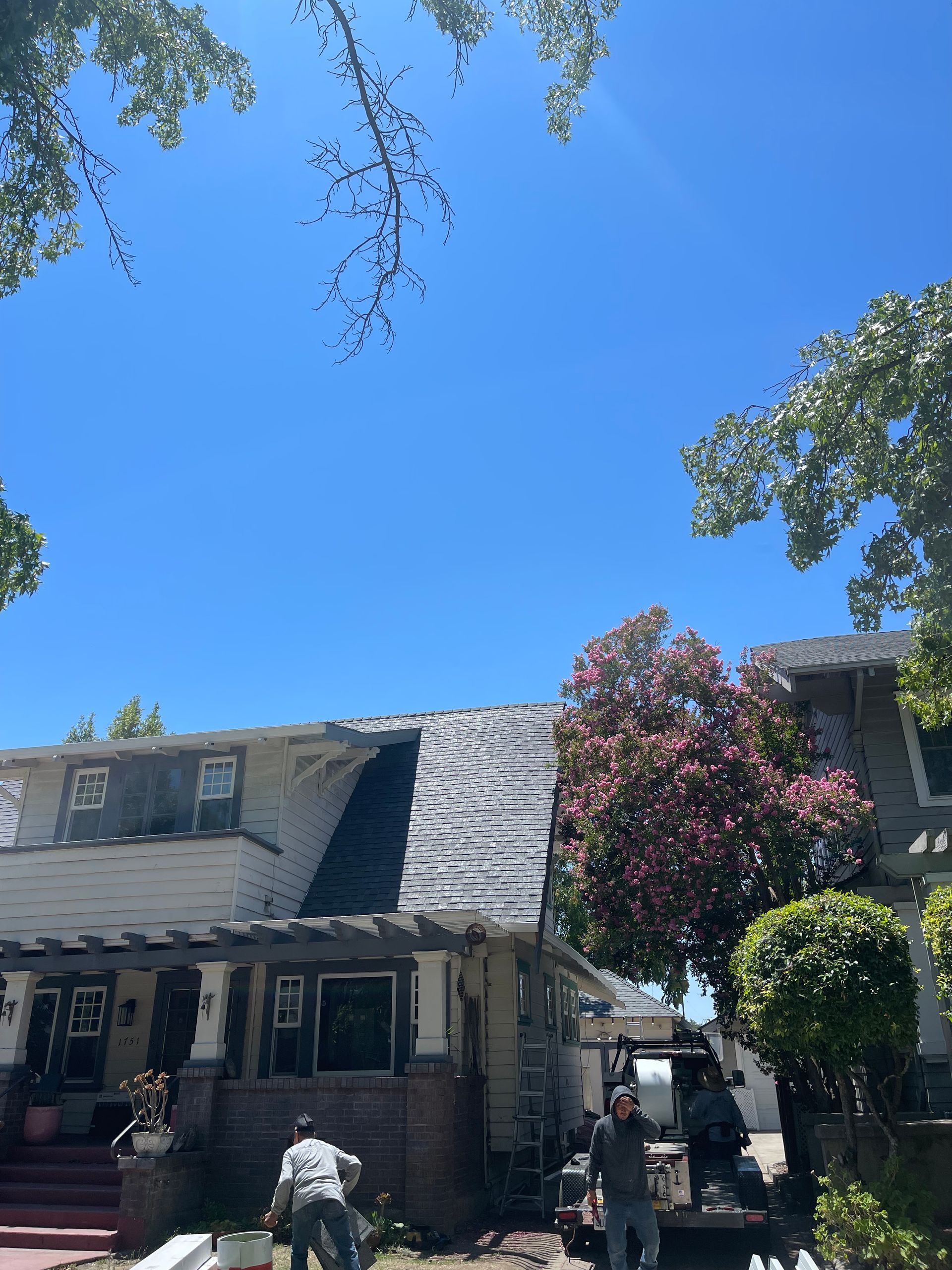 Residential house with gray roof and trees under a bright blue sky, with a person standing near the driveway