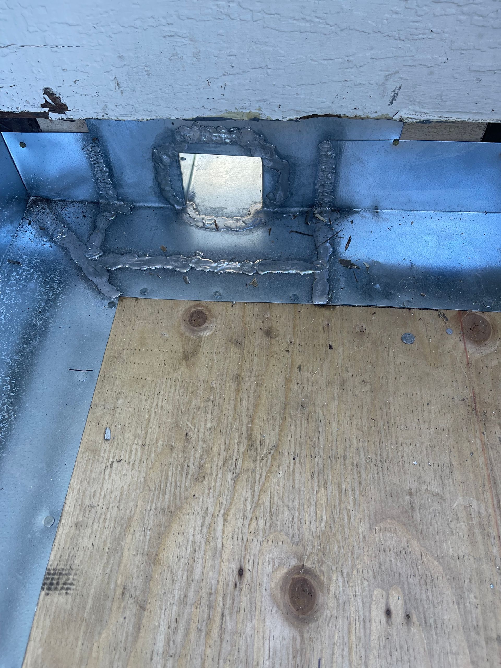 Blue metal corner with a small white vent above a plywood floor.
