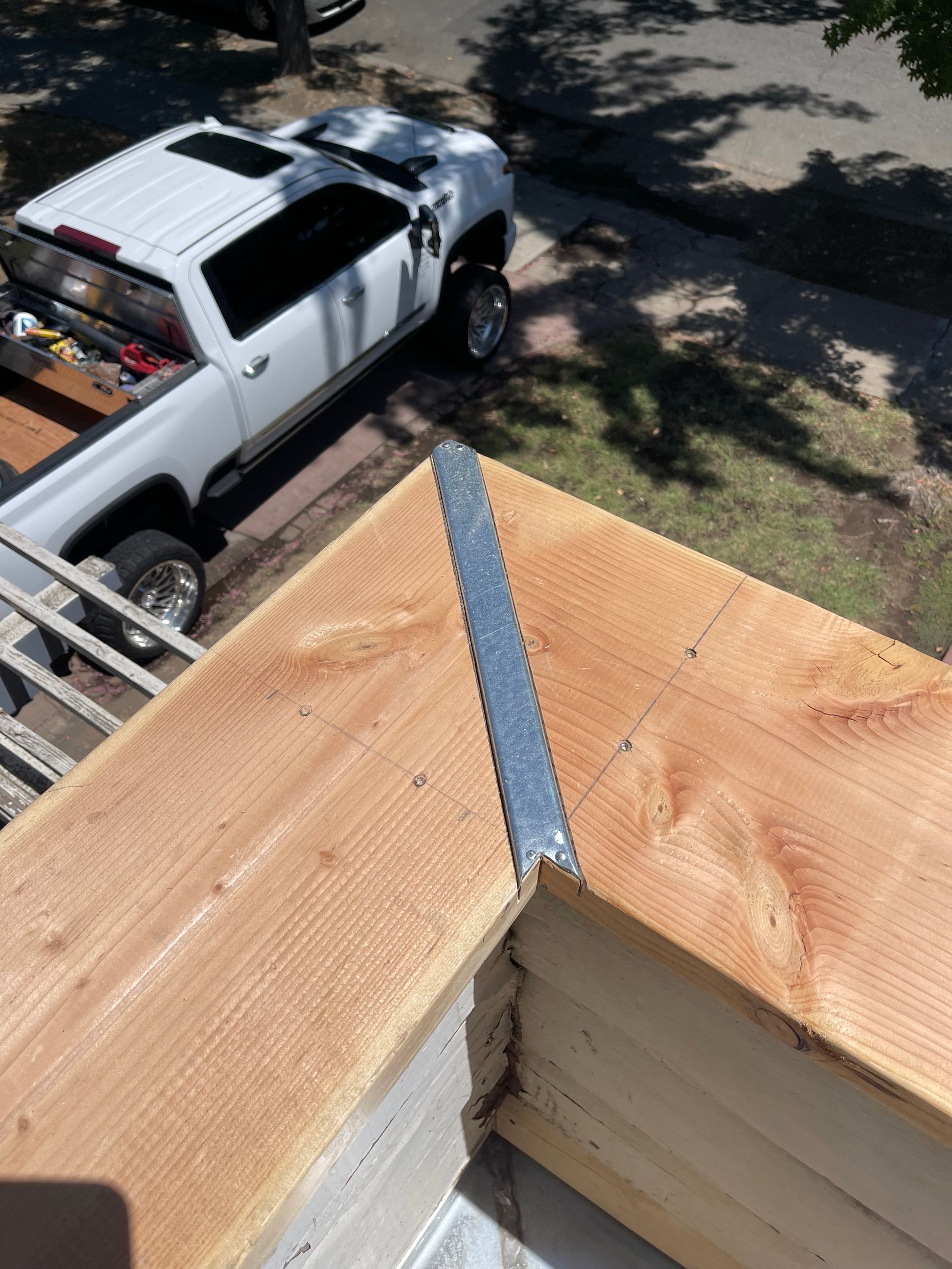 Roof corner with metal flashing; a white pickup truck and ladder are visible below.