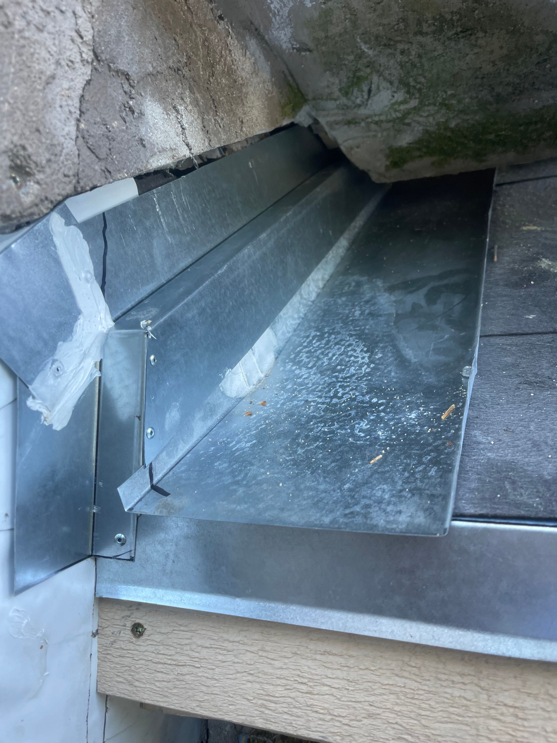 Metal chute inside a rock opening, with a dust-covered slanted trough and beige ledge below