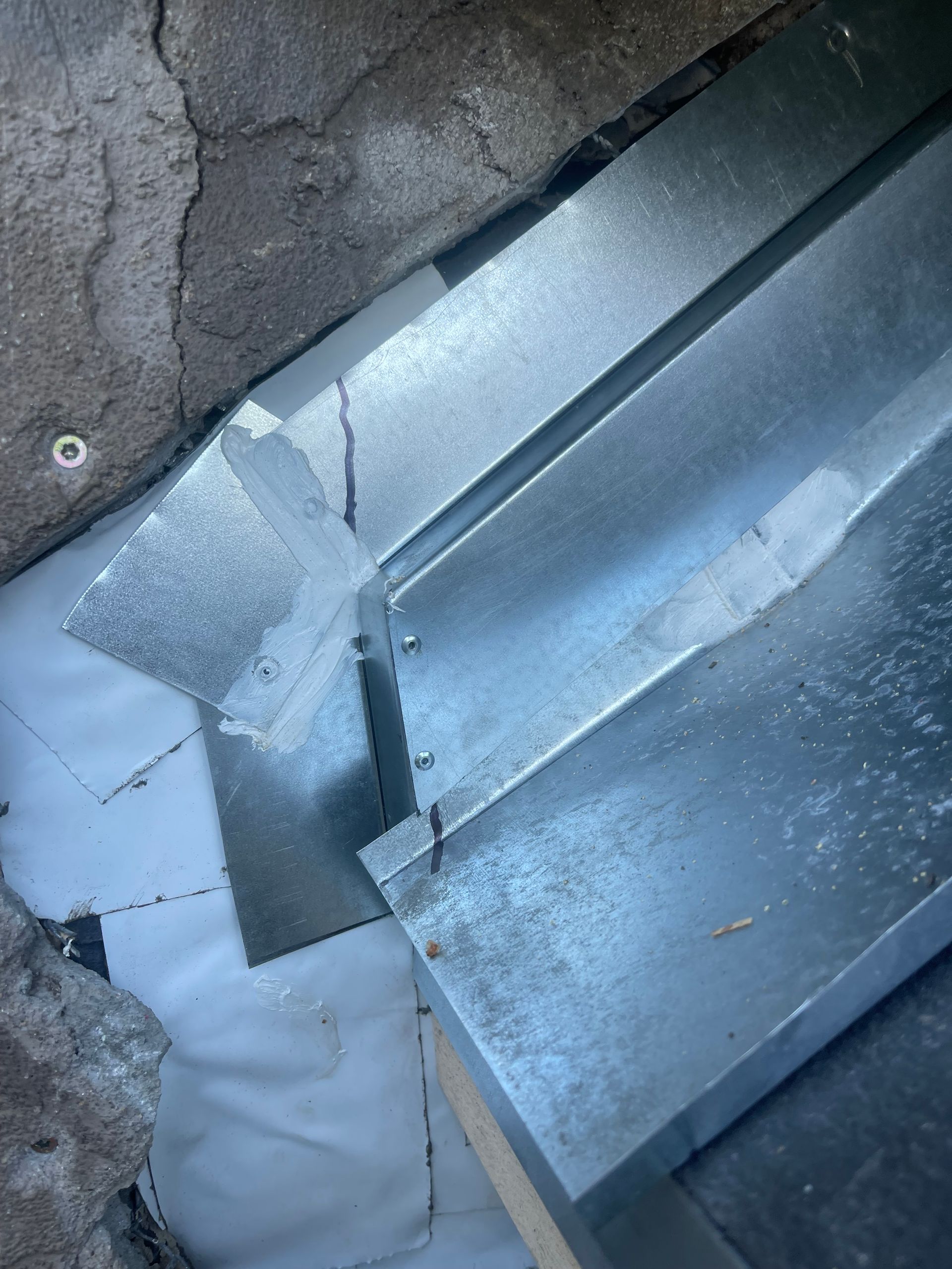 Close-up of damaged metal roofing with bent panels and exposed seams against cracked pavement.