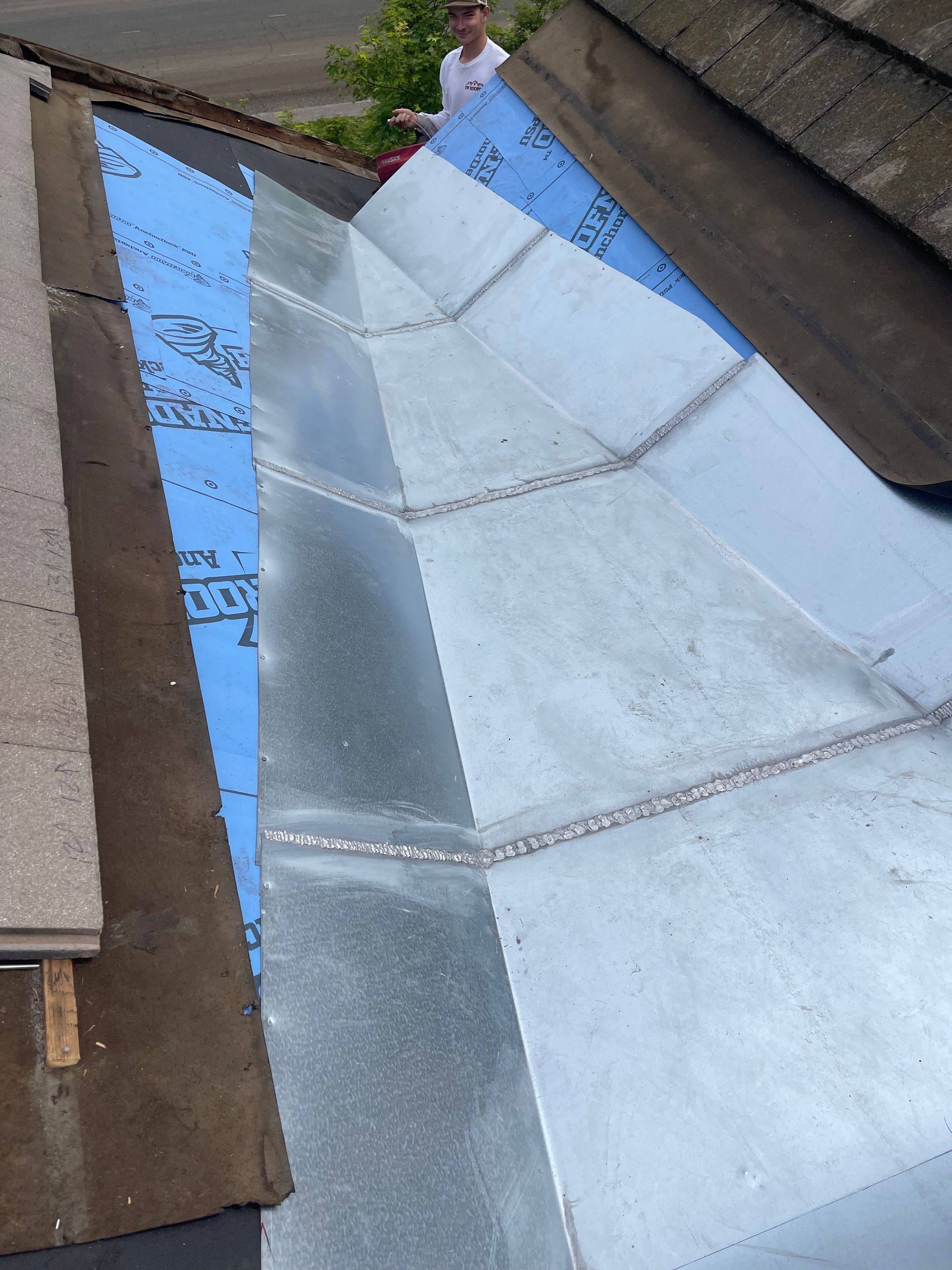 Blue-gray metal roof valley with seams between brown shingle roofs