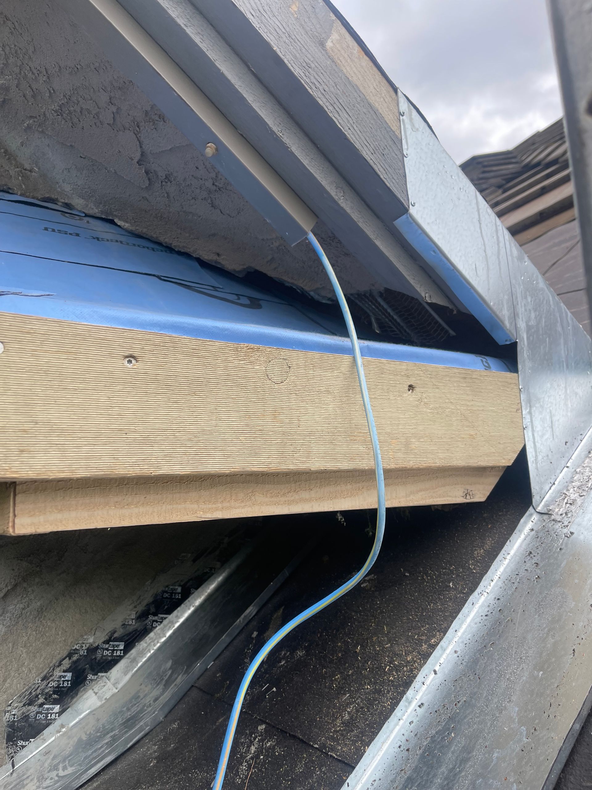 Close-up of layered roofing materials with a blue cable running between metal and wood surfaces.