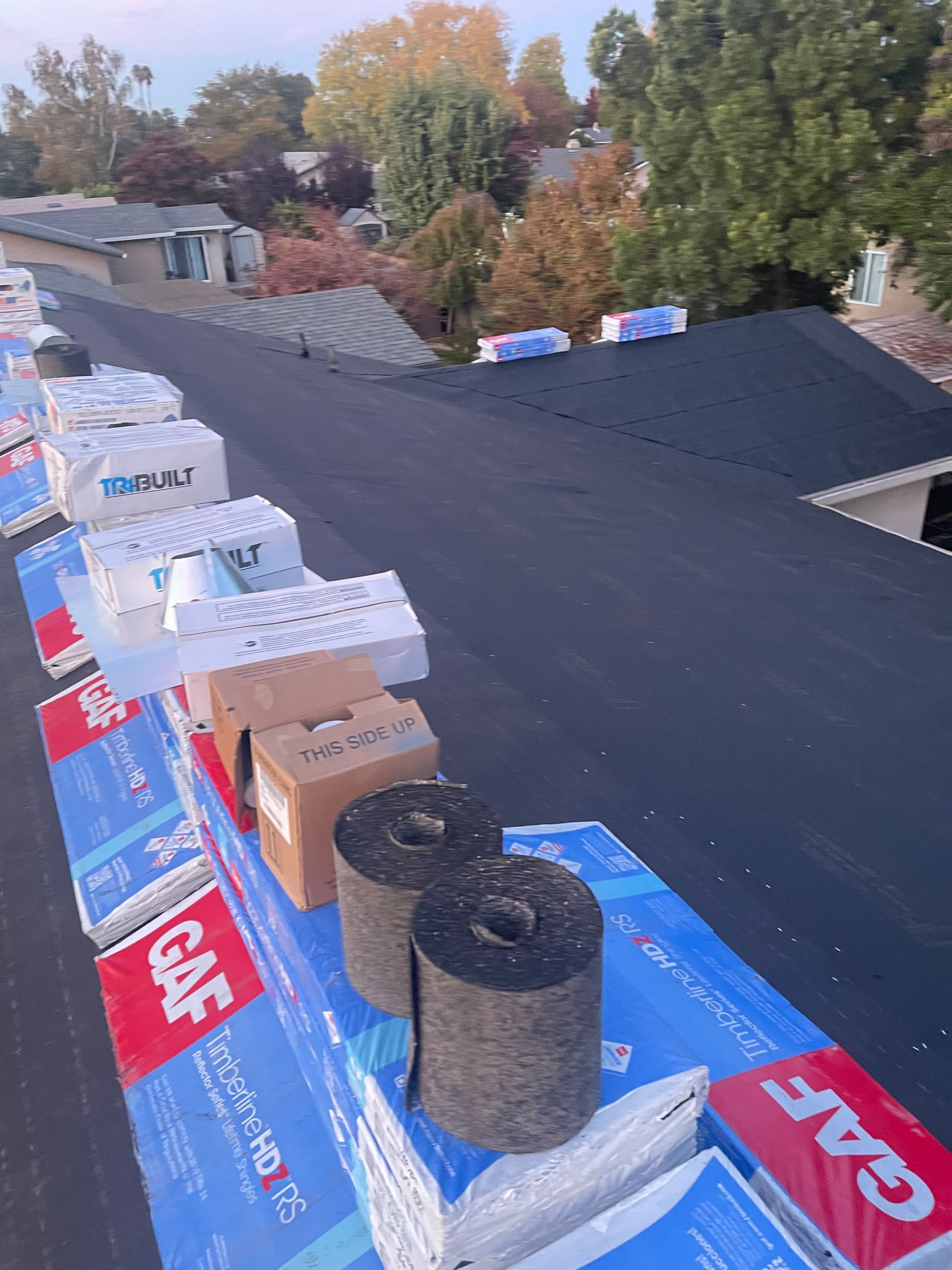 Roof under repair with rows of roofing materials, shingles, and underlayment on a dark rooftop.