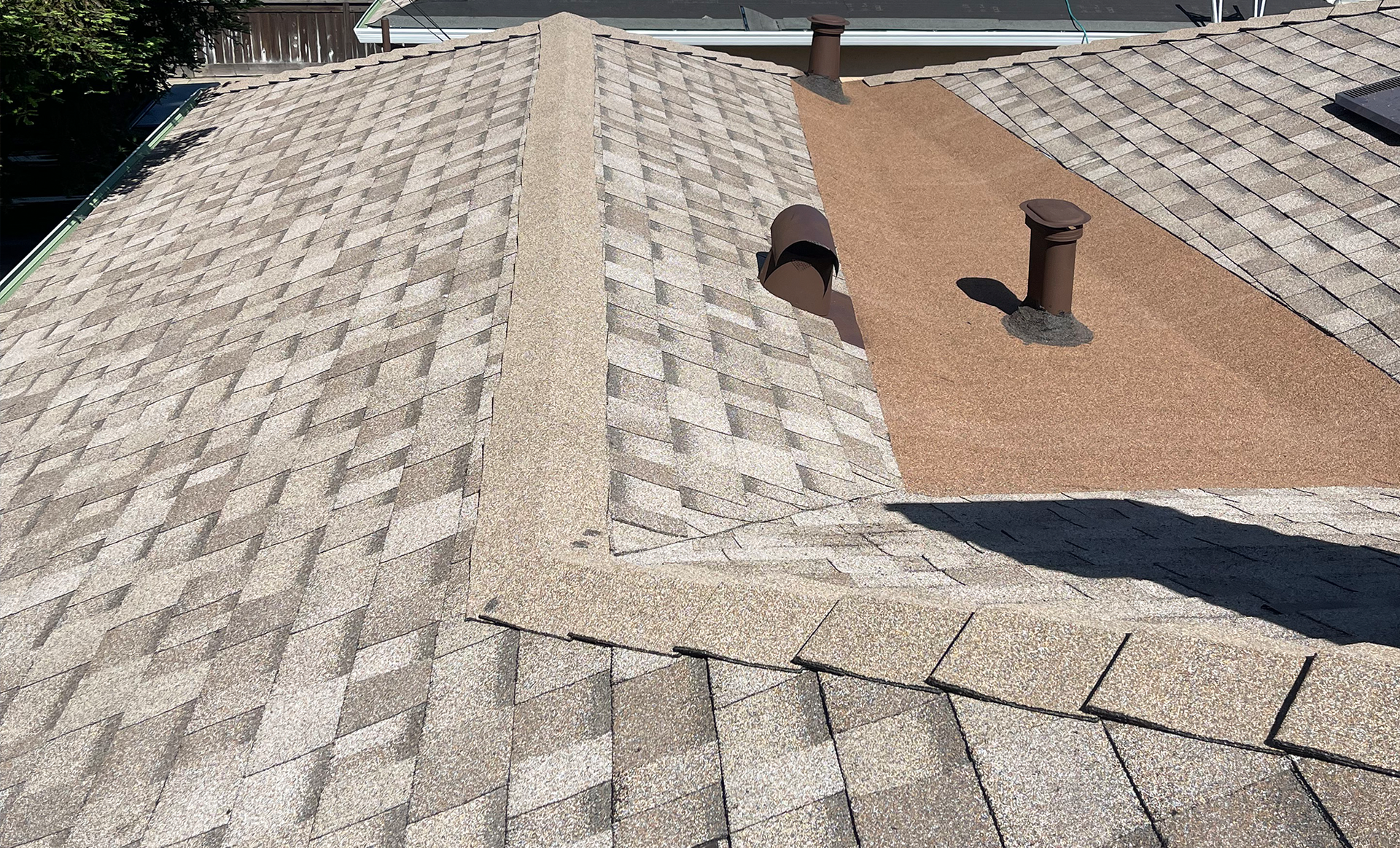 Rooftop with light gray shingles, a tan vent area, and two roof vents under bright sunlight