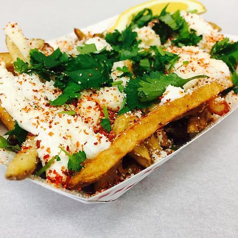 Loaded fries in a paper tray, topped with cilantro, cheese, and a lemon wedge.