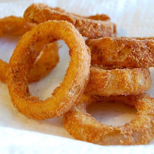 Golden, crispy fried onion rings on a white paper towel.
