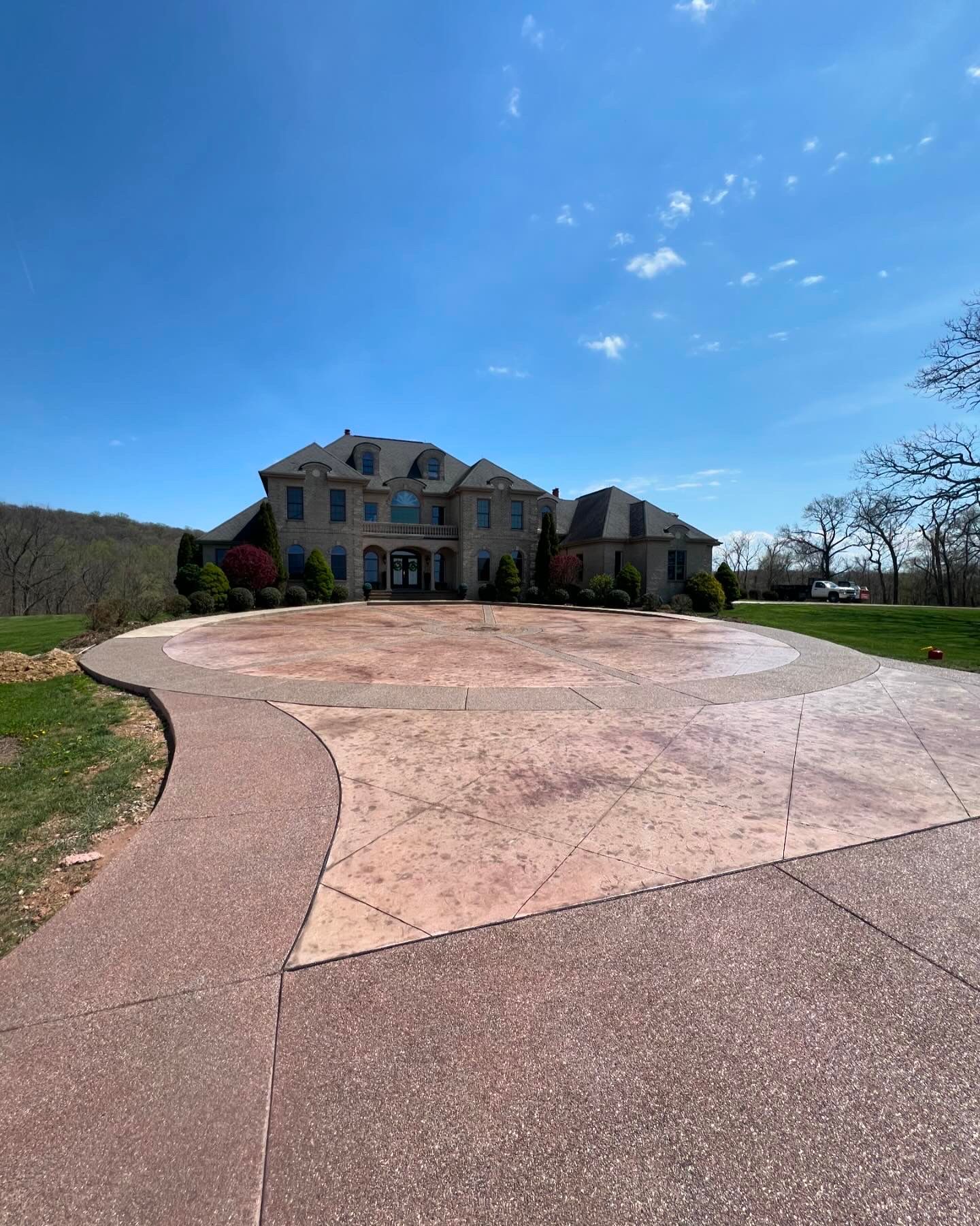 Large suburban house at the end of a curved driveway under a bright blue sky