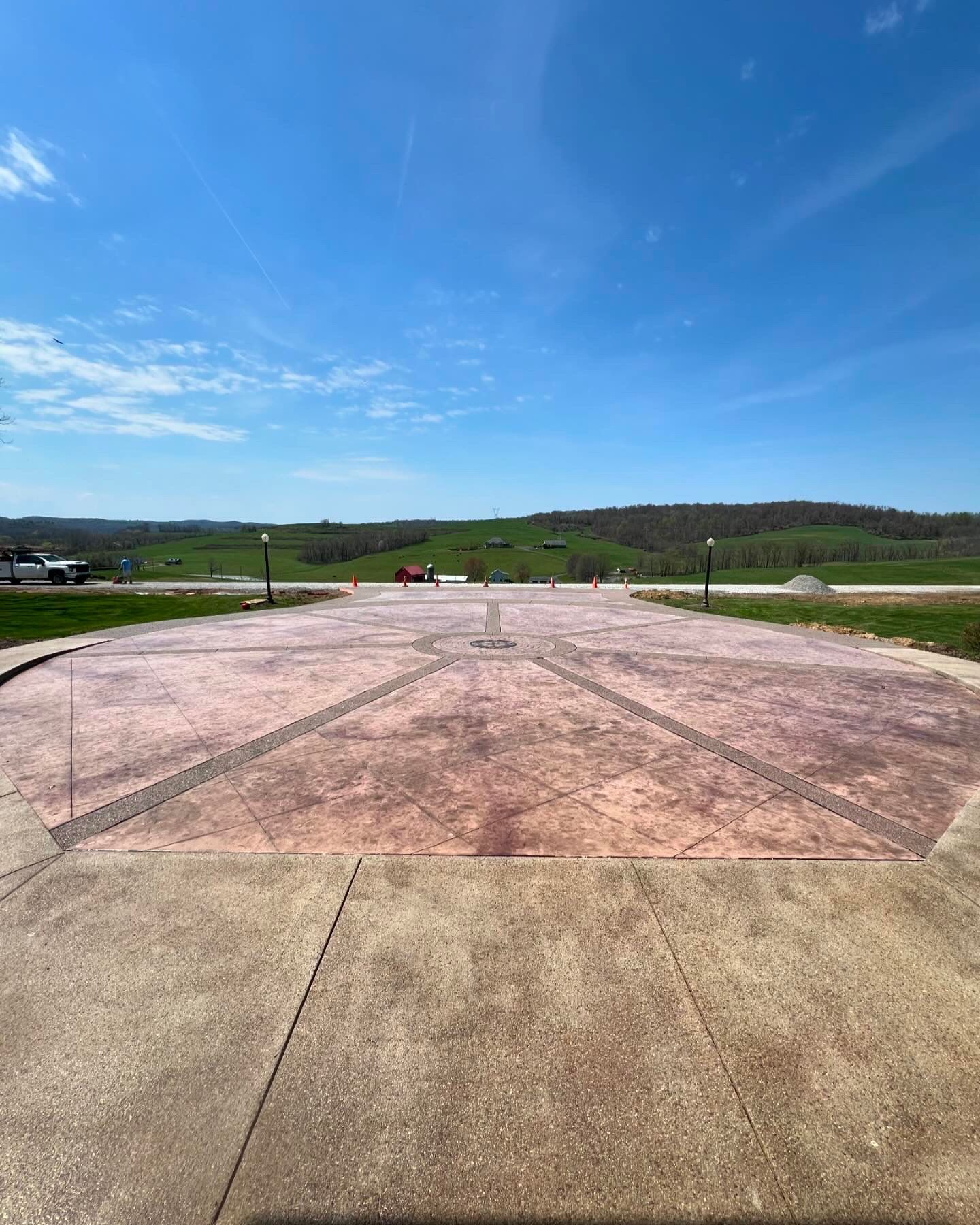 Wide concrete overlook with a pink-tinted center, under a bright blue sky and green hills in the distance