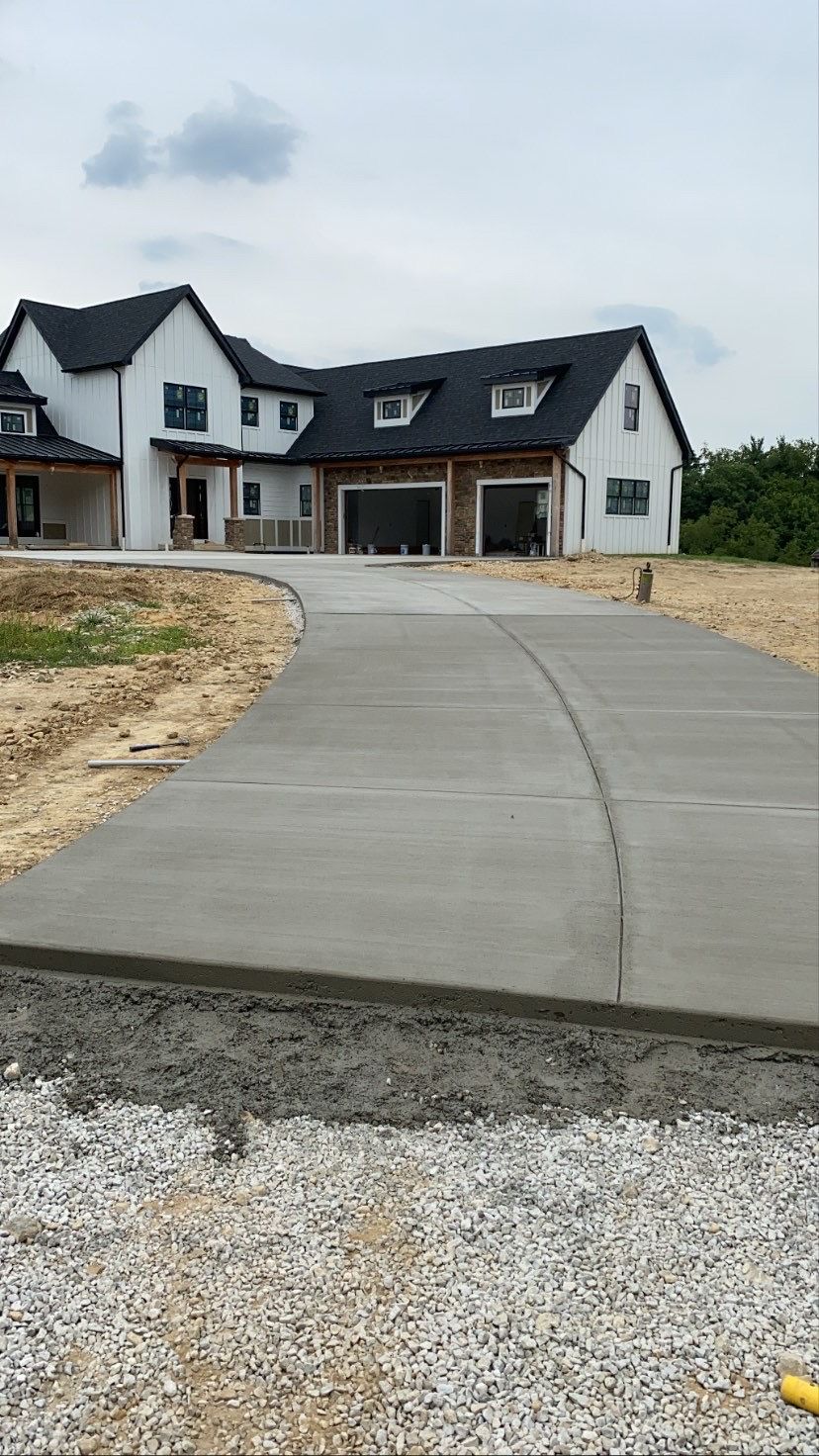 New concrete driveway leading to a large gray house under construction on a gravel lot