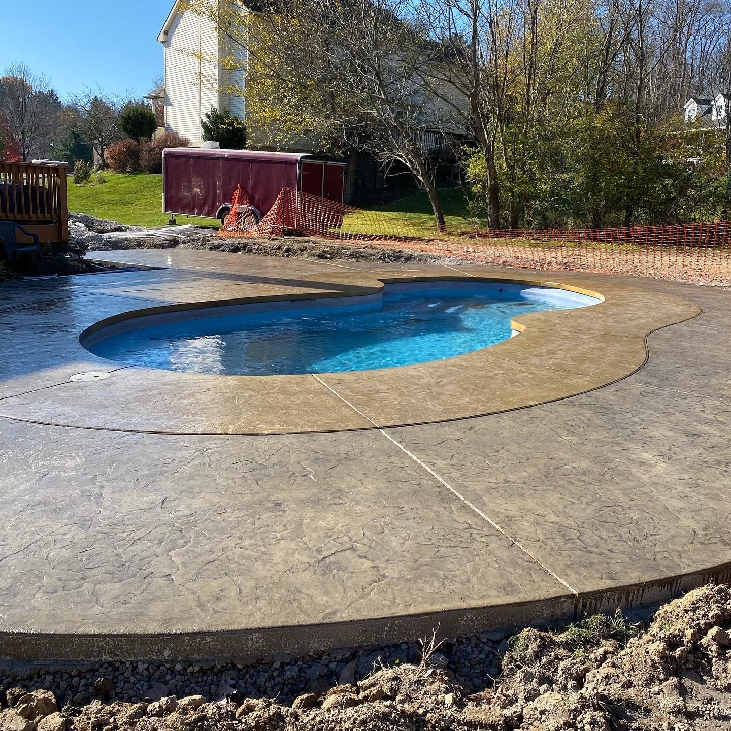 Small backyard pool with blue water set in a stamped concrete patio, surrounded by grass and trees.
