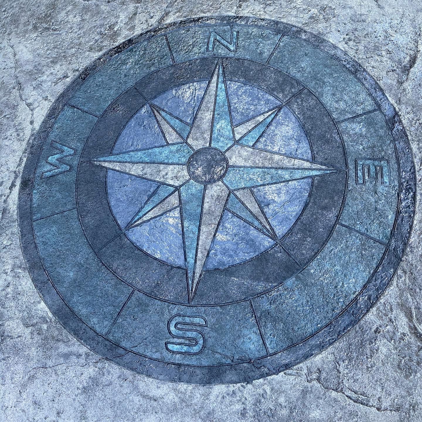 Blue compass rose emblem on a stone surface, with an “S” at the bottom and a small “III” on the right.