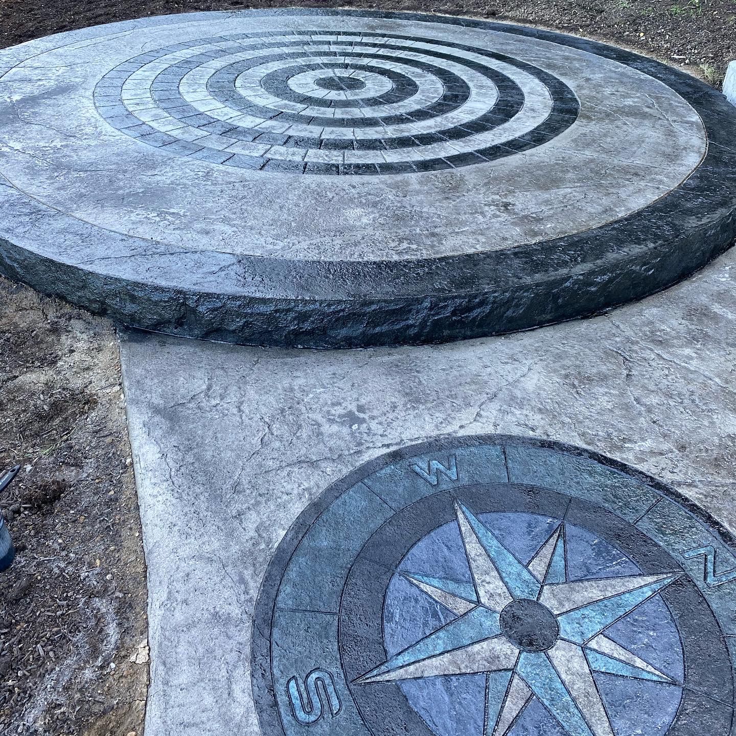 Stone patio with two circular inlaid designs: a black-and-white spiral and a blue compass rose.
