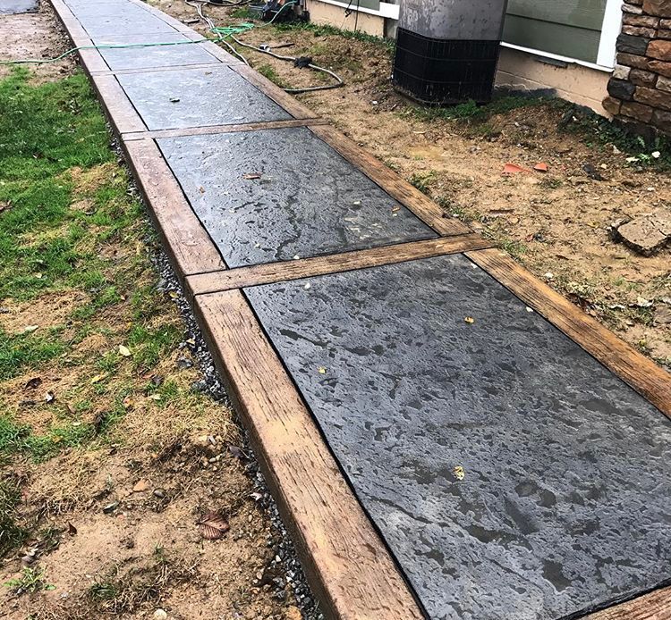 Uneven concrete walkway with wooden borders beside a house and patchy grass