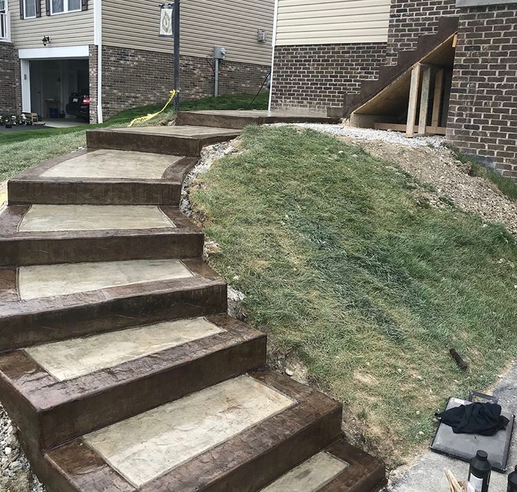 Outdoor concrete steps beside a sloped grassy yard next to a brick house and driveway.