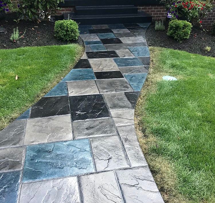 Colorful patterned stone walkway leading to a front porch, bordered by green lawn and shrubs.