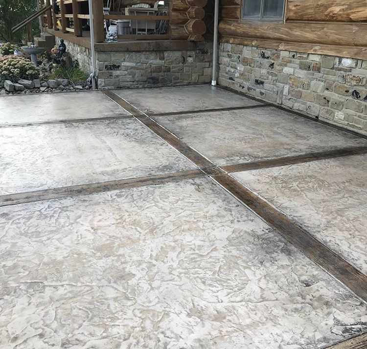 Concrete patio slabs beside a stone-and-wood house, with a small porch and rock garden edge