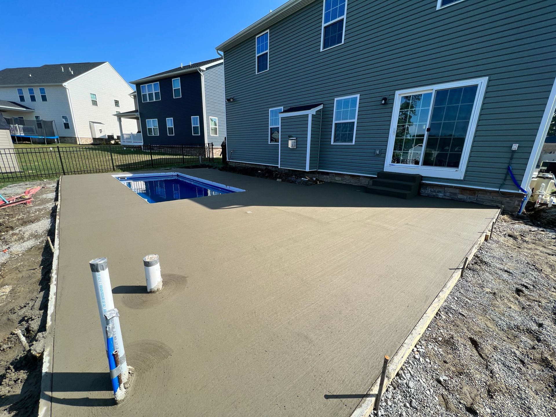 Backyard with a covered pool, tan patio, and blue-gray house siding.